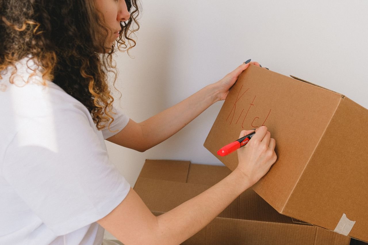 Woman organizing and labeling cardboard boxes for moving indoors.